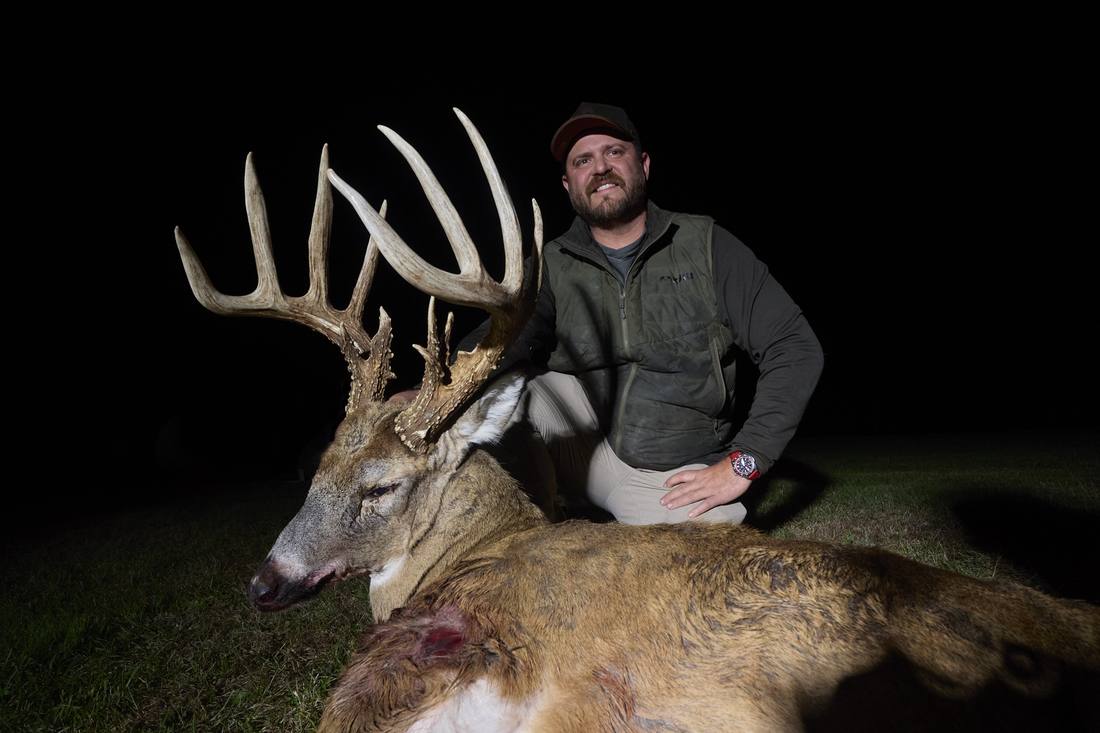 Hunter kneeling behind a tall-tined whitetail buck