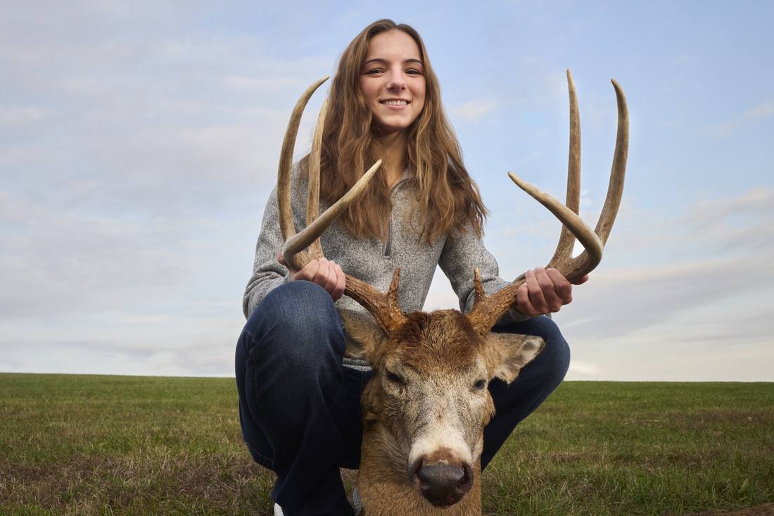 Young hunter holding the antlers of her buck in a field